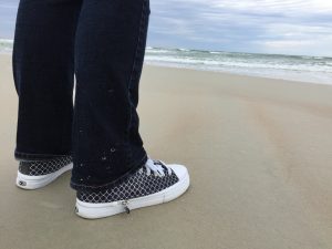 A photograph of my White Quarterfoil Pattern Black Background Zipz shoes at the Beach